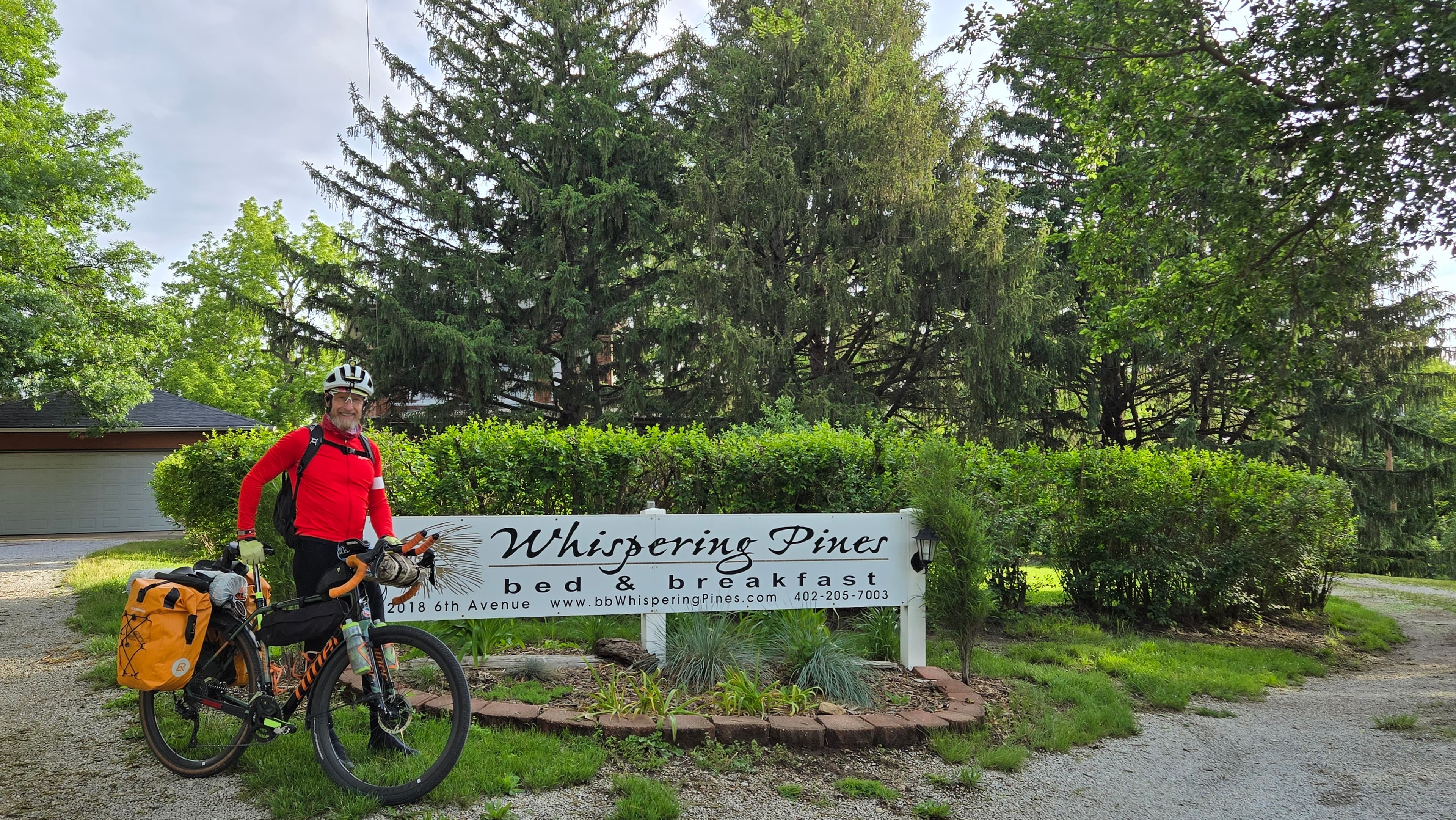 Cyclist Gary stands beside his loaded touring bicycle in front of the Whispering Pines Bed & Breakfast sign in Nebraska City, Nebraska. Cyclist Gary stands beside his loaded touring bicycle in front of the Whispering Pines Bed & Breakfast sign in Nebraska City, Nebraska.