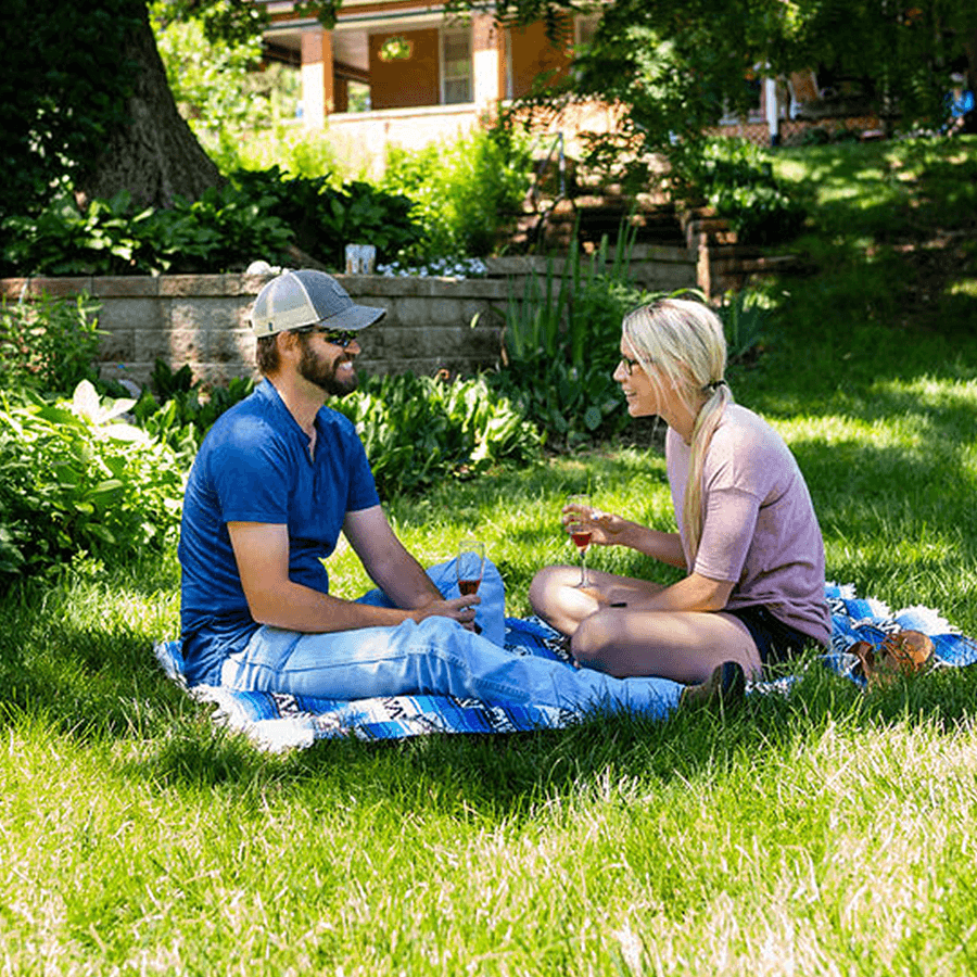 Man an woman sitting on a blanket in the yard under a tree on green grass drink red wine