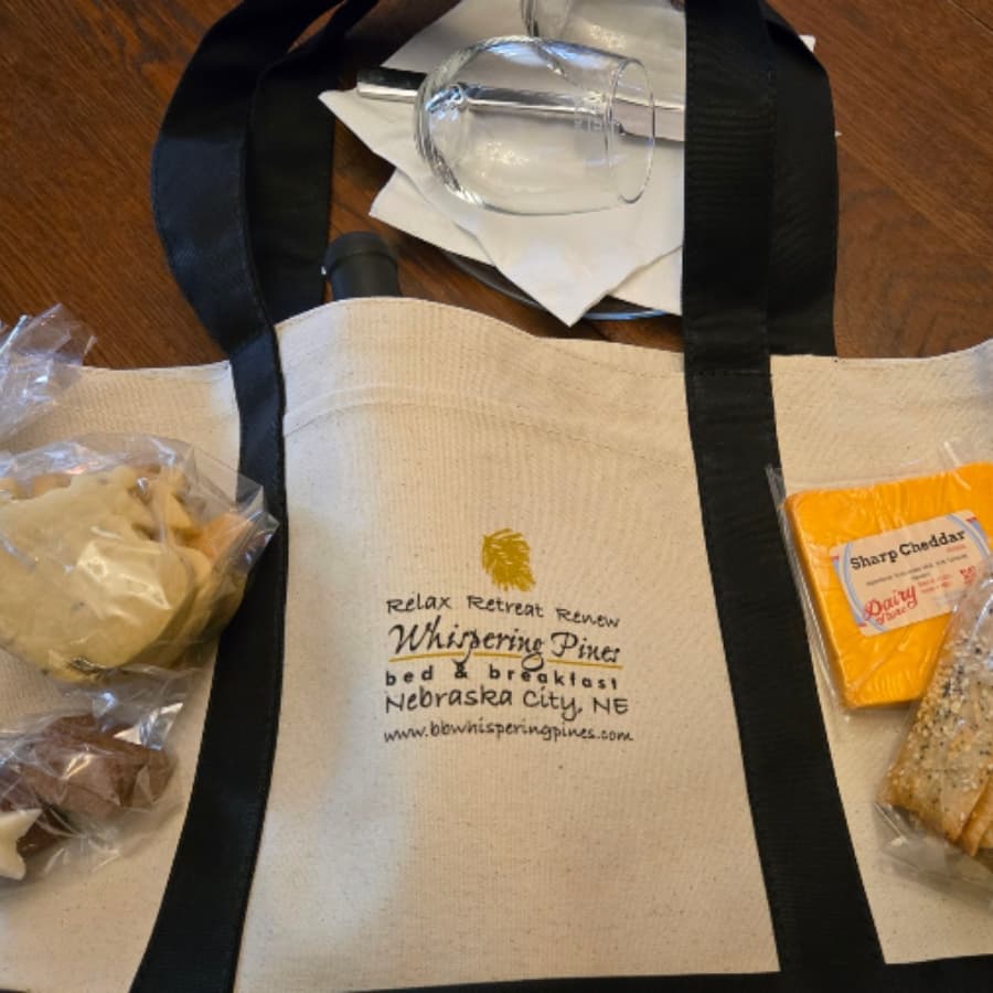 A canvas tote bag featuring treats, including cookies and cheese, from Whispering Pines Bed and Breakfast in Nebraska City.
